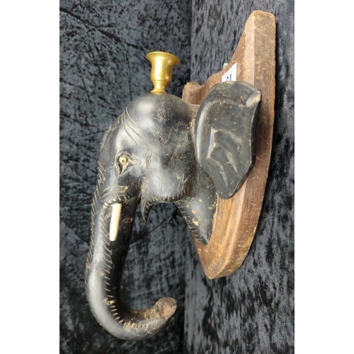 64 - Anglo-Indian carved ebony elephant head wall plaque, on a mahogany backboard and brass candle holder... 