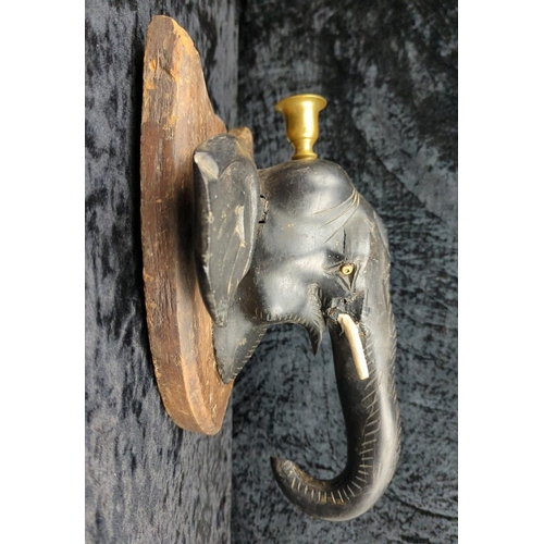 64 - Anglo-Indian carved ebony elephant head wall plaque, on a mahogany backboard and brass candle holder... 
