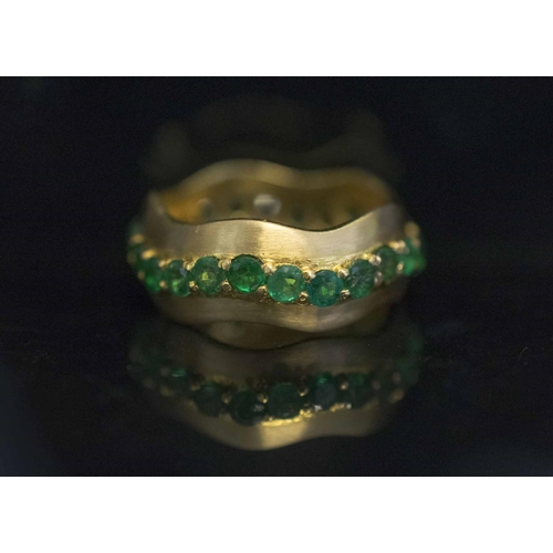 423 - AN EIGHTEEN CARAT GOLD AND EMERALD BAND RING, set with a wavy band of circular cut emeralds to the s... 