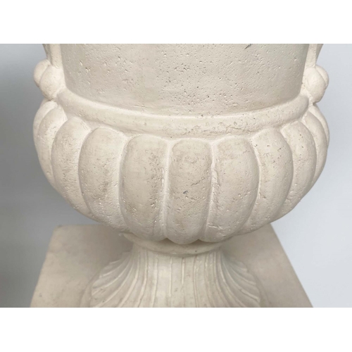 171 - URNS ON STANDS, a pair, campana form stone effect on plinths, 46cm W x 135cm H.