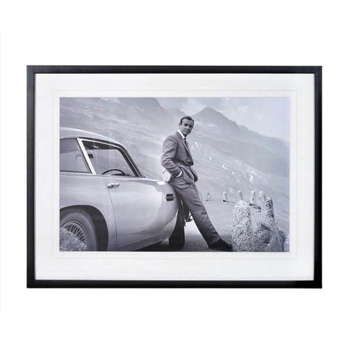 376 - SEAN CONNERY AS JAMES BOND with his Aston Martin, framed and glazed, 63cm x 83cm.