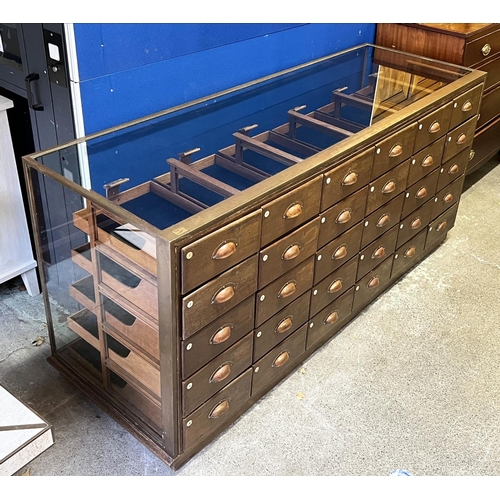 547 - HABERDASHERY COUNTER, oak and bronze framed with glass sides and back with an arrangement of 30 draw... 