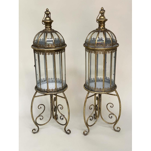 127 - STORM LANTERNS ON STAND, a pair, metal and glazed with handles and scroll supports, 106cm H. (2)