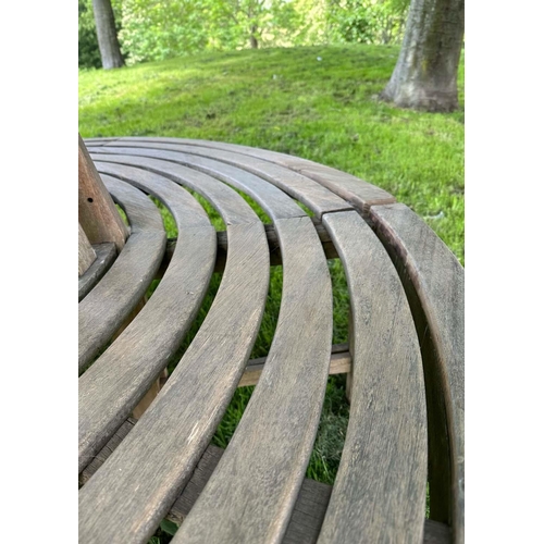 181 - GARDEN TREE BENCH, weathered teak in two sections, with slatted upstand and concentric slatted seat,... 