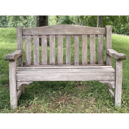 495 - GARDEN BENCH, weathered teak of slatted and pegged construction with flat top arms and arched back, ... 