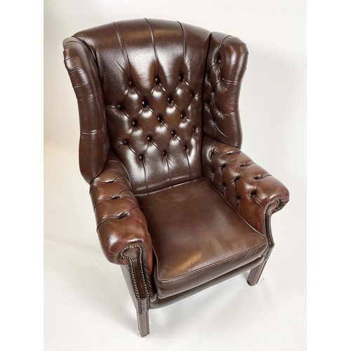 169 - WING ARMCHAIR, deep buttoned brown leather, with brass stud work and stretchered legs with buttoned ... 