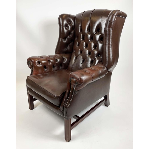 169 - WING ARMCHAIR, deep buttoned brown leather, with brass stud work and stretchered legs with buttoned ... 