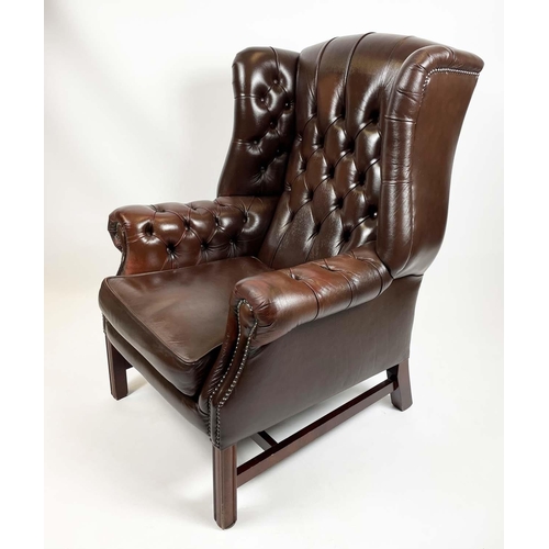 169 - WING ARMCHAIR, deep buttoned brown leather, with brass stud work and stretchered legs with buttoned ... 