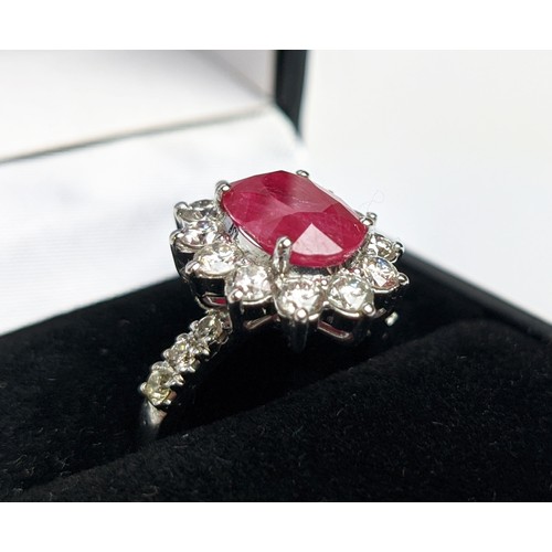 47 - AN 18CT WHITE GOLD RUBY AND DIAMOND CLUSTER RING, with diamond set shoulders, the central oval cut r... 