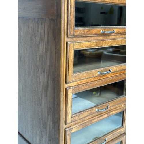 246 - HABERDASHERY CABINET BY DUDLEY & CO, mid 20th century oak with sixteen glazed drawers above two slid... 