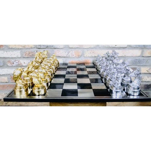 657 - CHESS SET, chequered board complete with silvered and gilt finish animal form pieces, 60cm x 60cm.