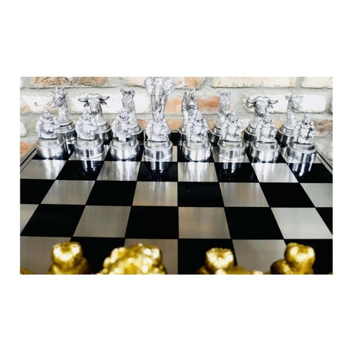 657 - CHESS SET, chequered board complete with silvered and gilt finish animal form pieces, 60cm x 60cm.