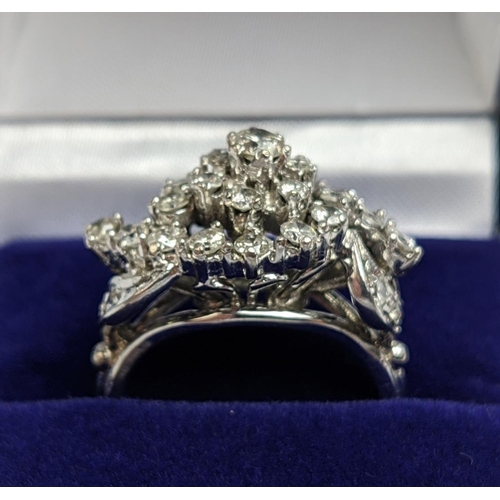 31 - A WHITE METAL AND DIAMOND CLUSTER RING, the centre with a flower head setting surrounded by C scroll... 