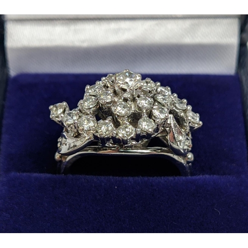 31 - A WHITE METAL AND DIAMOND CLUSTER RING, the centre with a flower head setting surrounded by C scroll... 