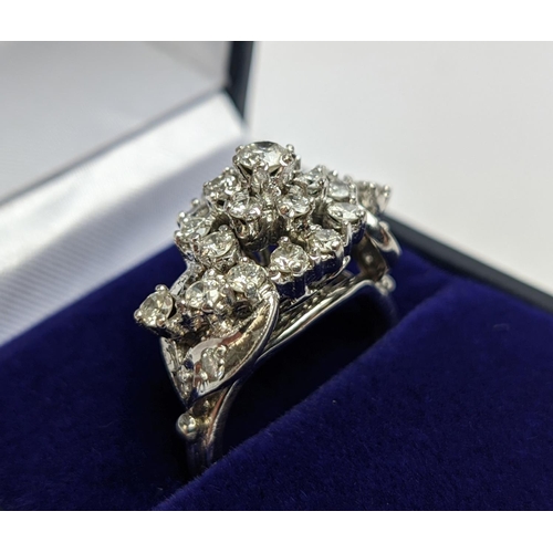 31 - A WHITE METAL AND DIAMOND CLUSTER RING, the centre with a flower head setting surrounded by C scroll... 