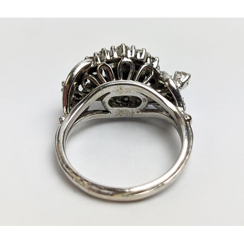 31 - A WHITE METAL AND DIAMOND CLUSTER RING, the centre with a flower head setting surrounded by C scroll... 