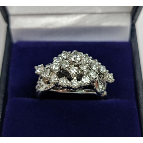 31 - A WHITE METAL AND DIAMOND CLUSTER RING, the centre with a flower head setting surrounded by C scroll... 