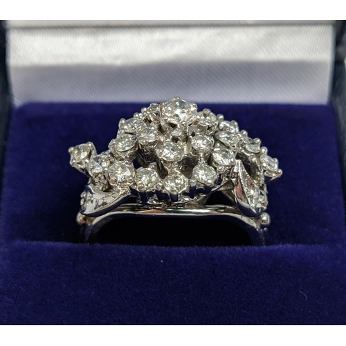 58 - A WHITE METAL AND DIAMOND CLUSTER RING, the centre with a flower head setting surrounded by C scroll... 