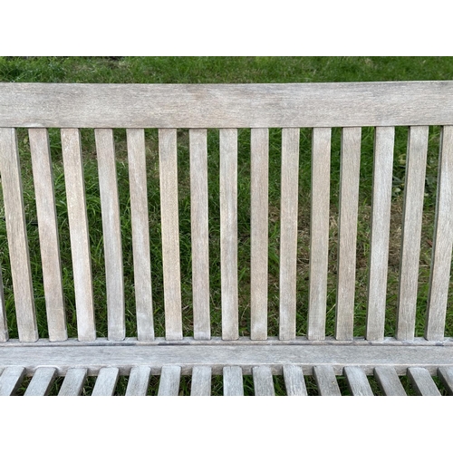 129 - GARDEN BENCH, weathered teak of slatted construction with slightly arch shaped back and curved arms,... 