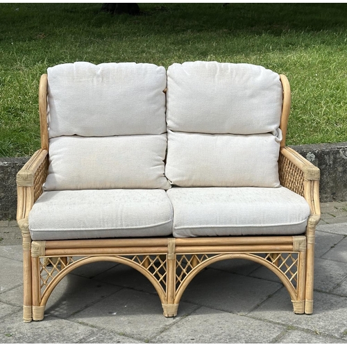 487 - ORANGERY STYLE SOFA, wingback rattan framed and cane bound, two seater with trellis sides and cushio... 