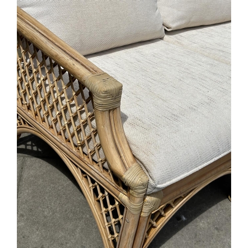 487 - ORANGERY STYLE SOFA, wingback rattan framed and cane bound, two seater with trellis sides and cushio... 