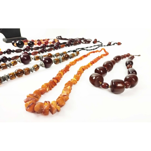 12 - A QUANTITY OF ASSORTED AMBER COLOURED BEAD NECKLACES, some glass and some in plastic, in red and ora... 