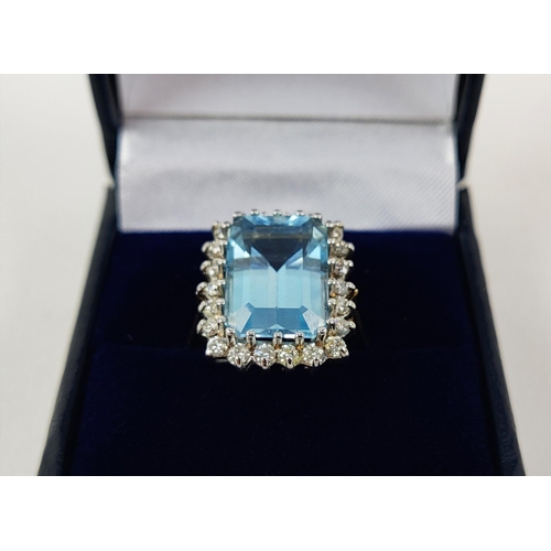 20 - AN 18CT GOLD SWISS BLUE TOPAZ AND DIAMOND RING, the emerald cut topaz surrounded by 22 round brillia... 