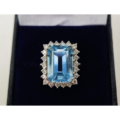 20 - AN 18CT GOLD SWISS BLUE TOPAZ AND DIAMOND RING, the emerald cut topaz surrounded by 22 round brillia... 