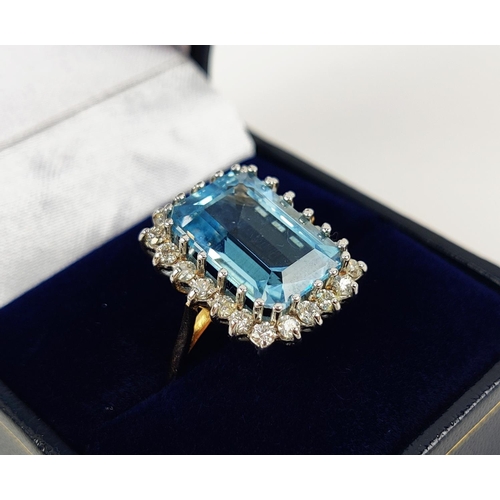 20 - AN 18CT GOLD SWISS BLUE TOPAZ AND DIAMOND RING, the emerald cut topaz surrounded by 22 round brillia... 