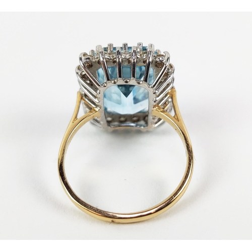 20 - AN 18CT GOLD SWISS BLUE TOPAZ AND DIAMOND RING, the emerald cut topaz surrounded by 22 round brillia... 