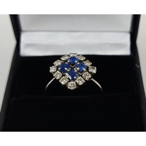 23 - A WHITE METAL DIAMOND AND SAPPHIRE SQUARE SET CLUSTER RING, with four sapphires surrounded by a halo... 