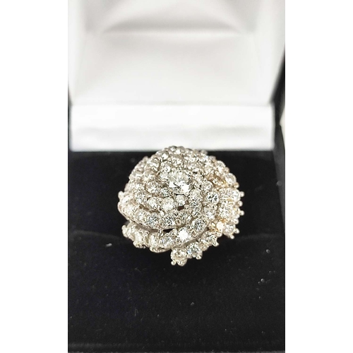 26 - AN 18CT WHITE GOLD DIAMOND CLUSTER RING, in a swirl design, the central round brilliant cut stone of... 