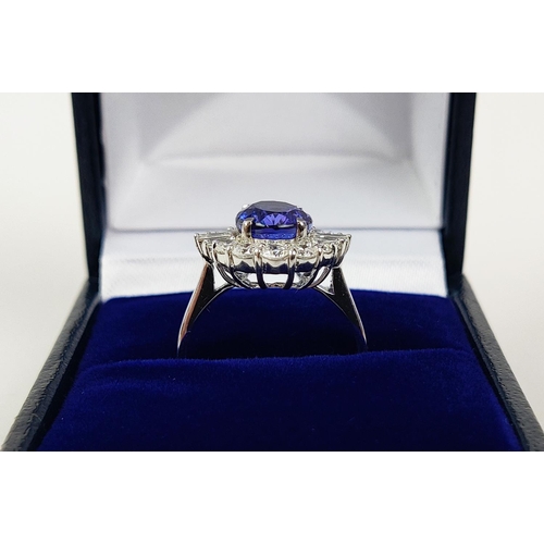 12 - AN 18CT WHITE GOLD TANZANITE AND DIAMOND DRESS RING, the central tanzanite stone surrounded by brill... 