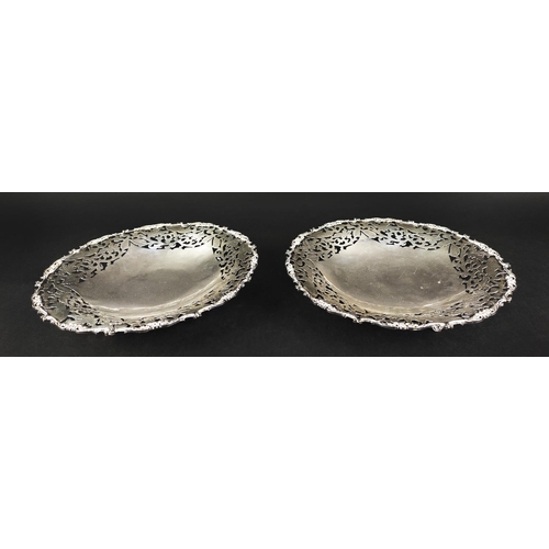 10 - A PAIR OF WHITE METAL PIERCED DISHES, raised on three feet, scrollwork borders, 29cm diameter, total... 