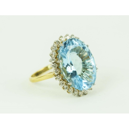 AN 18CT YELLOW GOLD TOPAZ AND DIAMOND DRESS RING, the oval blue topaz of approximately 10 carats, surrounded by a halo of diamonds, ring size O, complete with box