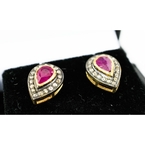 28 - A PAIR OF RUBY AND DIAMOND STUD EARRINGS, each with a pair shaped faceted ruby surrounded by a borde... 