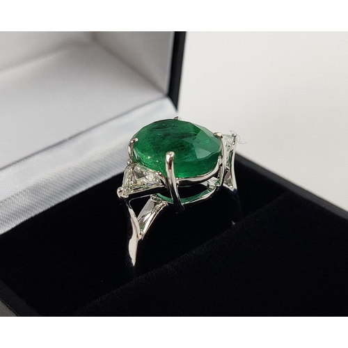 24 - AN 18CT WHITE GOLD EMERALD AND DIAMOND RING, the central oval cut emerald flanked by trilliant cut d... 