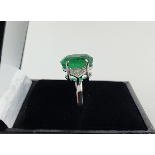 24 - AN 18CT WHITE GOLD EMERALD AND DIAMOND RING, the central oval cut emerald flanked by trilliant cut d... 