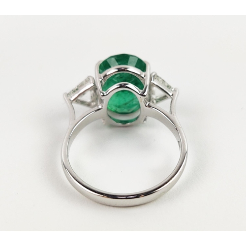 24 - AN 18CT WHITE GOLD EMERALD AND DIAMOND RING, the central oval cut emerald flanked by trilliant cut d... 