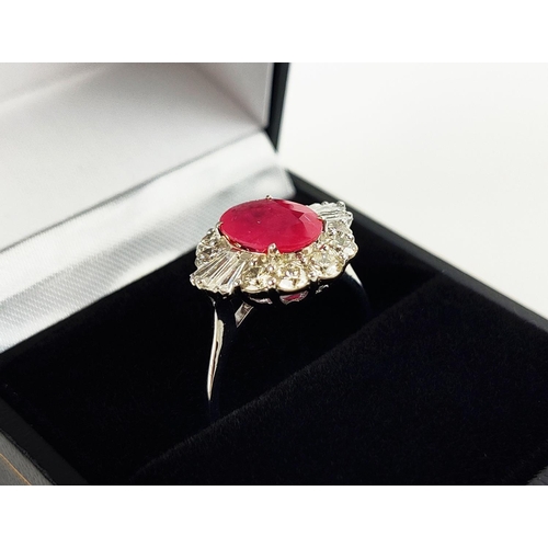 28 - A 18CT WHITE GOLD RUBY AND DIAMOND RING, the oval mixed cut ruby surrounded by a halo of round brill... 