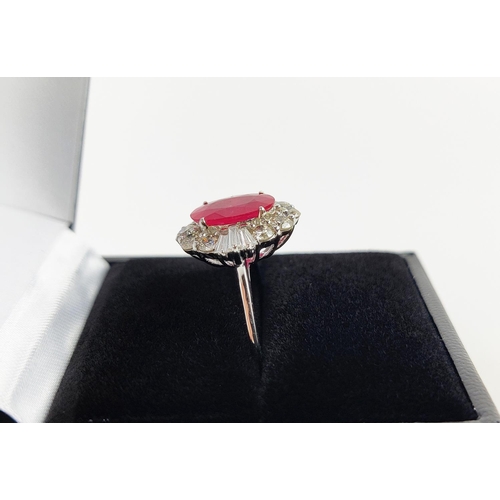 28 - A 18CT WHITE GOLD RUBY AND DIAMOND RING, the oval mixed cut ruby surrounded by a halo of round brill... 