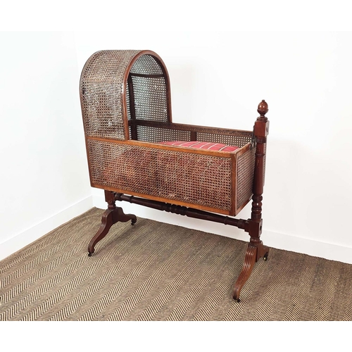 359 - CRADLE, George IV mahogany and caned with pine slatted base, check cushion and brass castors, 136cm ... 