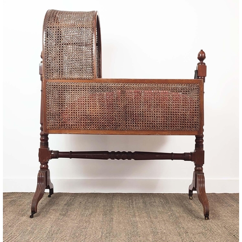 359 - CRADLE, George IV mahogany and caned with pine slatted base, check cushion and brass castors, 136cm ... 