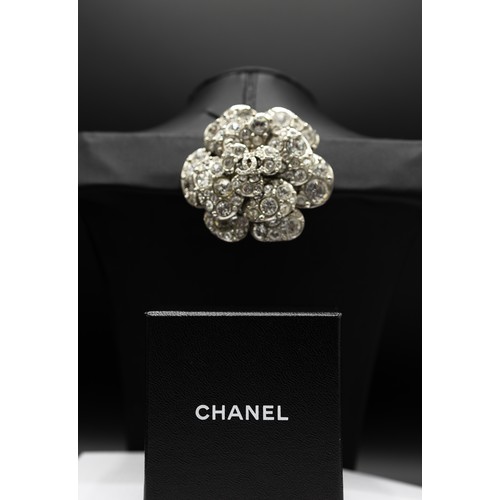 17A - CHANEL BROOCH, iconic camellia flower with a central double CC logo, rhinestones and silver tone met... 