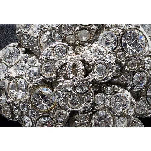 17A - CHANEL BROOCH, iconic camellia flower with a central double CC logo, rhinestones and silver tone met... 