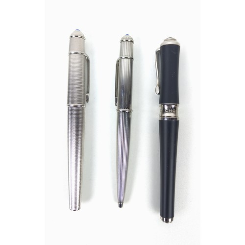 120A - TWO CARTIER BALLPOINT WHITE METAL PENS, comprising one with an engine turned case, blue cabochon ter... 