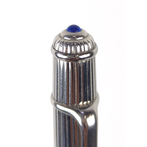 120A - TWO CARTIER BALLPOINT WHITE METAL PENS, comprising one with an engine turned case, blue cabochon ter... 