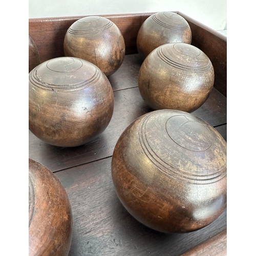 140 - BOWLS, a set of eight, vintage lignum vitae bowls in an old mahogany tray, tray 51cm x 46cm x 12cm.