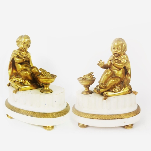 205B - A PAIR OF GILT BRONZE AND MARBLE CLOCK GARNITURES, in the form on putti on a plinth, 22cm high.