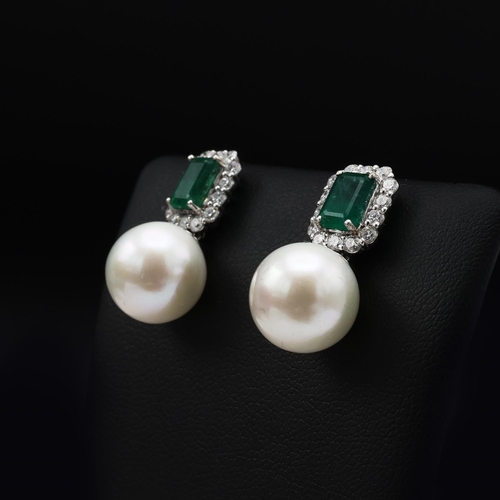 132 - A PAIR OF 18CT WHITE GOLD PEARL DROP EARRINGS, each set with a large emerald-cut emerald surrounded ... 